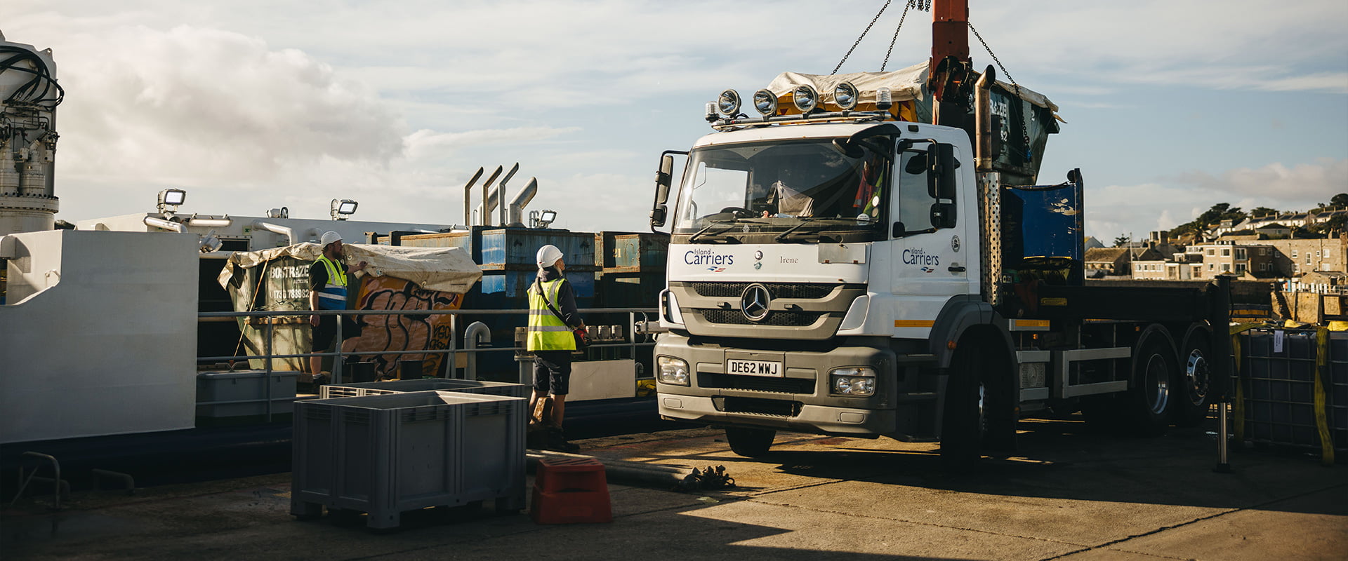Island carrier lorry using crane to unload skip, next to Menawethan, St Mary's quay